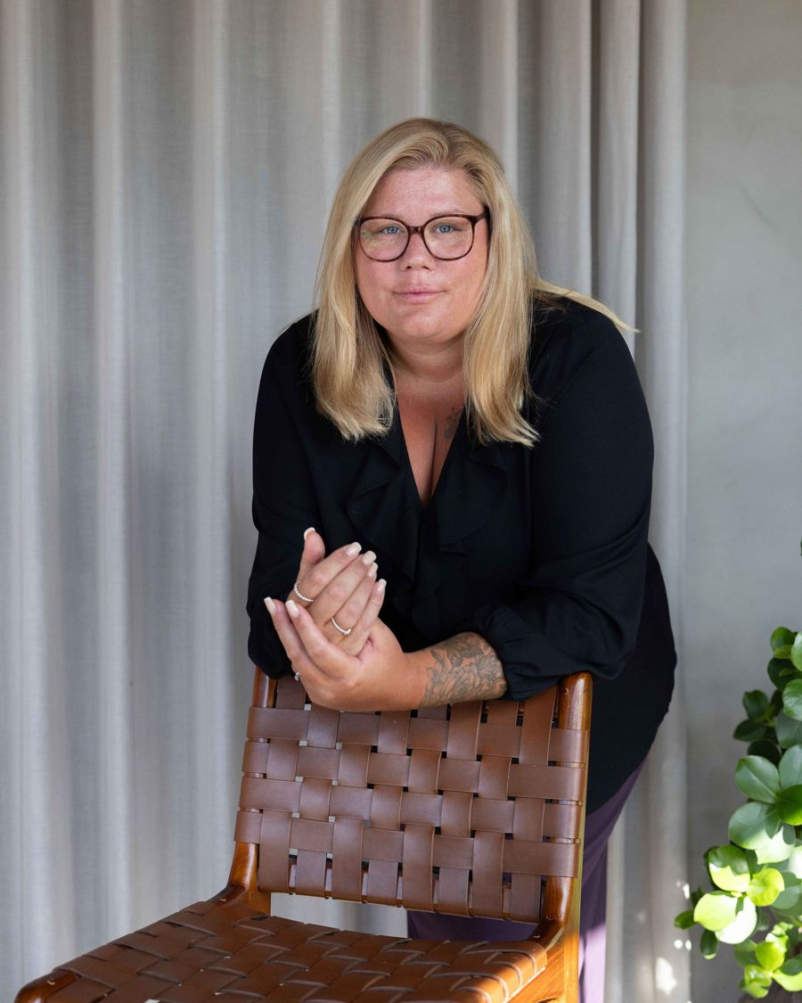 Nina lutar sig mot ryggstödet på en flätad läderstol.